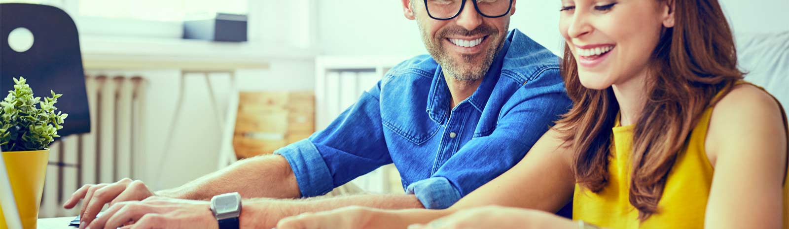 Couple smiling and sitting in front of laptop.